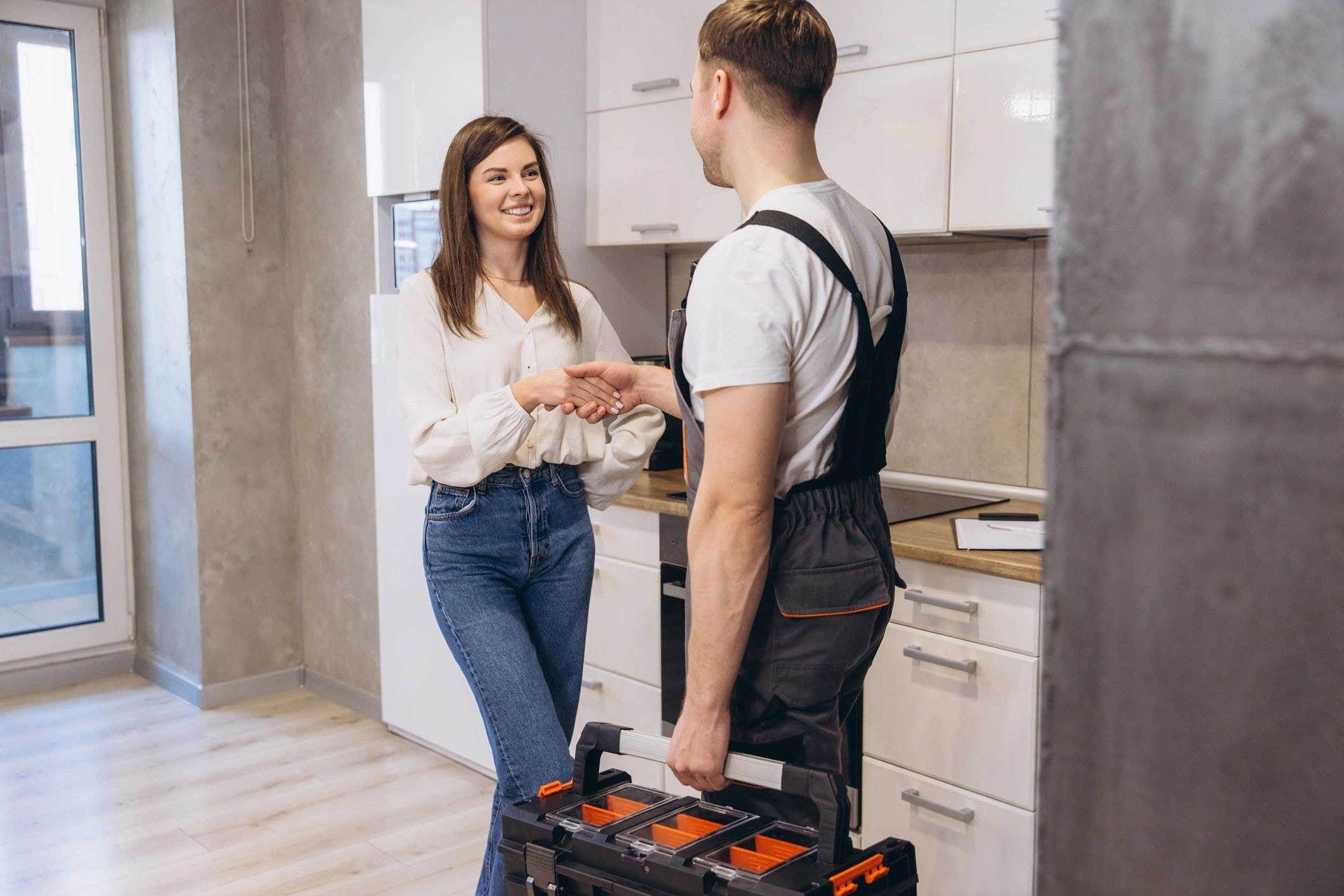 A smiling woman shaking hands with a workman carrying a toolbox in a modern kitchen